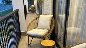 Een balkon met rieten meubels, waaronder een stoel en een bank, en een klein houten krukje.