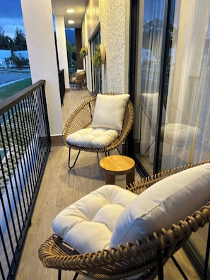 A balcony with wicker furniture, including a chair and a sofa, and a small wooden stool. - Soreli•Peaceful Retreat at Green One Playa Dorada (Puerto Plata city)