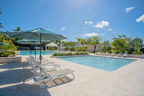 A pool area with lounge chairs and umbrellas. - Soreli•Peaceful Retreat at Green One Playa Dorada (Puerto Plata city)