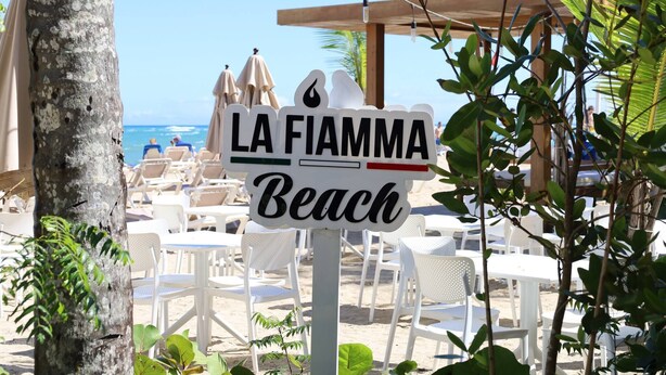 Een strandbordje met de tekst 'LA FIAMMA Beach', omringd door strandstoelen en parasols.