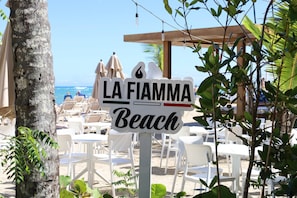A beach sign with 'LA FIAMMA Beach' written on it, surrounded by beach chairs and umbrellas.