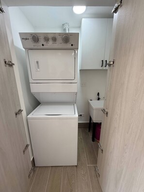 Ein kleiner Hauswirtschaftsraum mit platzsparender Waschmaschine und Trockner übereinander, einem kleinen Waschbecken und einem Schrank.