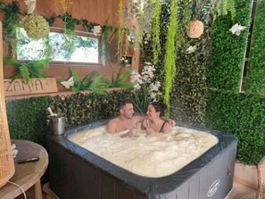 Un bain à remous agrémenté d’une pancarte en bois portant l’inscription « ZAMPA » et d’un mur en bois rustique orné de plantes et de fleurs.