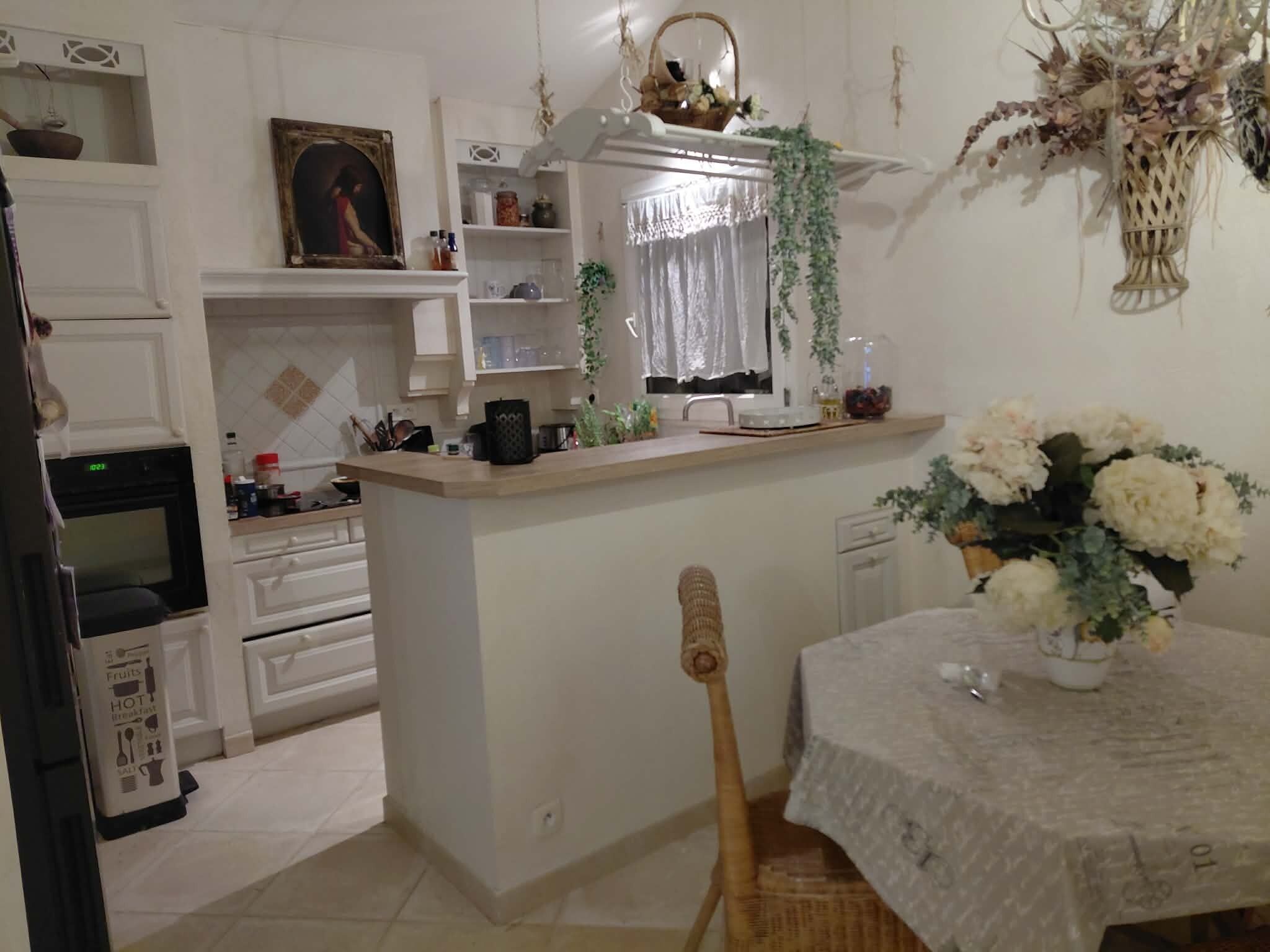 Et køkken med en central ø, et spisebord med en vase blomster og et ur på væggen.