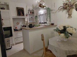 A kitchen with a central island, a dining table with a vase of flowers, and a clock on the wall. - KAZAMIA: Charm & romance—optional hot tub included on weekends (La Motte)