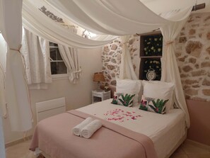 Une chambre avec un mur en pierre, un lit avec une literie rose, une table de chevet avec une lampe et une fenêtre avec des rideaux.