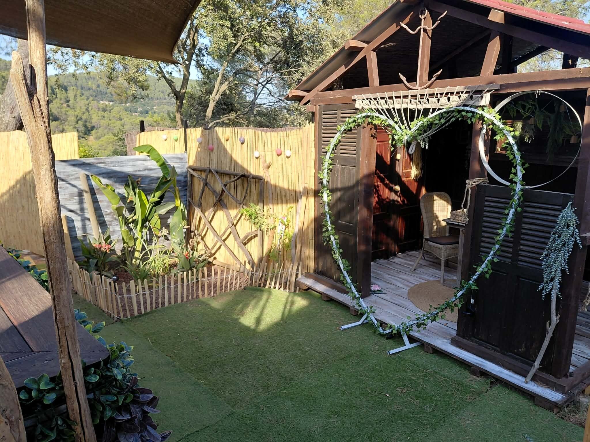 A wooden deck with a covered seating area, surrounded by a wooden fence and a garden with various plants.