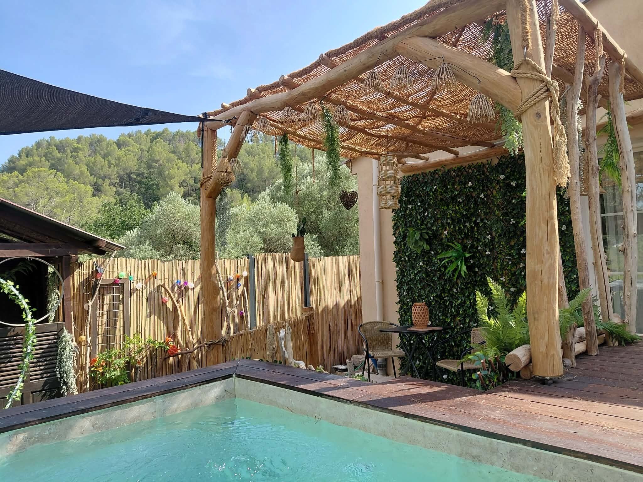 A pool area with a pergola, wooden deck, and a view of a forested hillside.