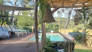 Et poolområde med jacuzzi, liggestole og en pergola med hængende lys.