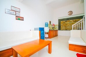 A living room with a white sofa, a wooden coffee table, and a staircase with a stone wall. - Cozzy Villa Andela (batu)