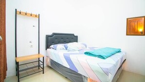 Ein Einzelbett mit grauem Kopfteil, eine Sitzbank und eine Wandleuchte.
