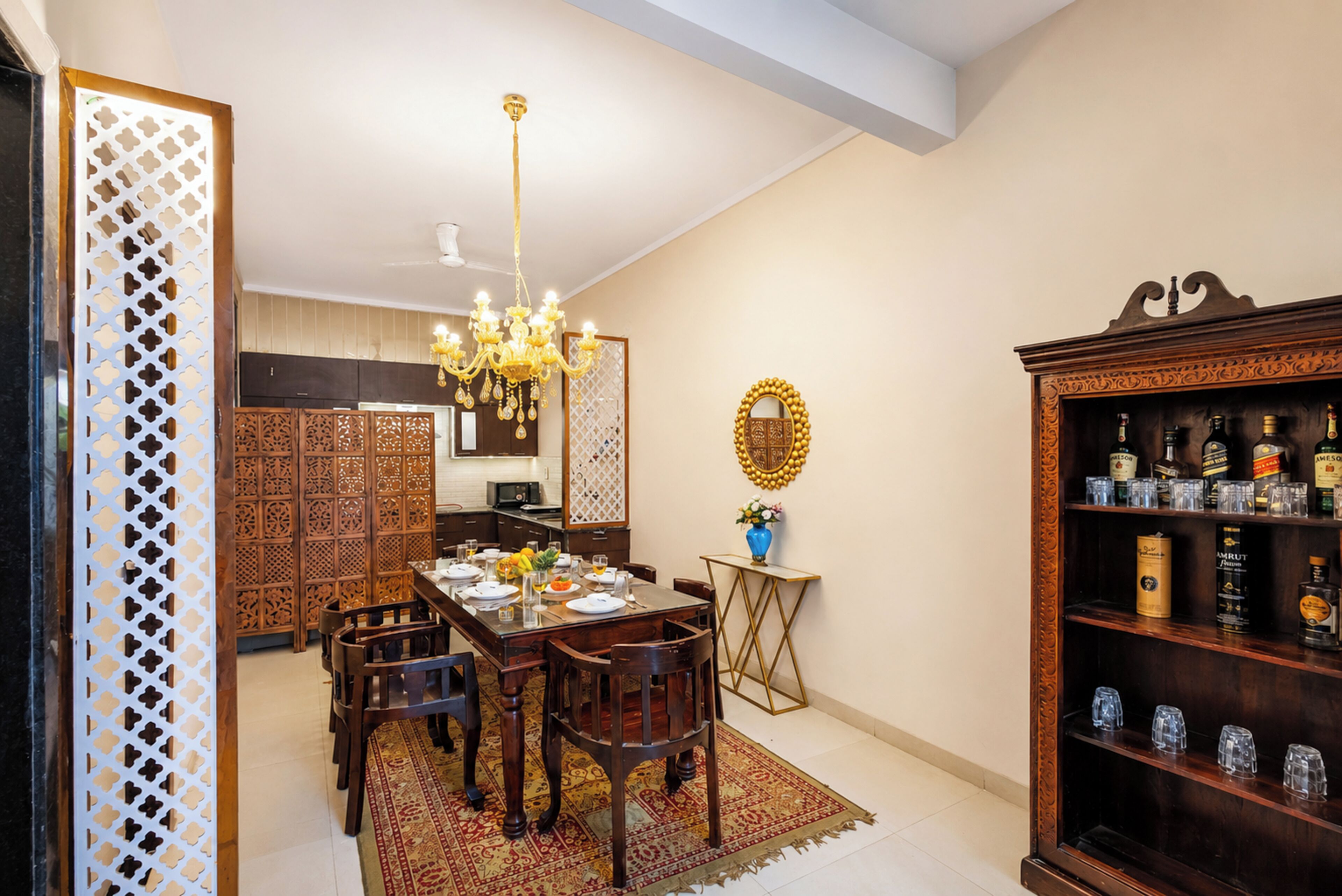 A dining area with a chandelier, a wooden cabinet with bottles, and a decorative mirror.