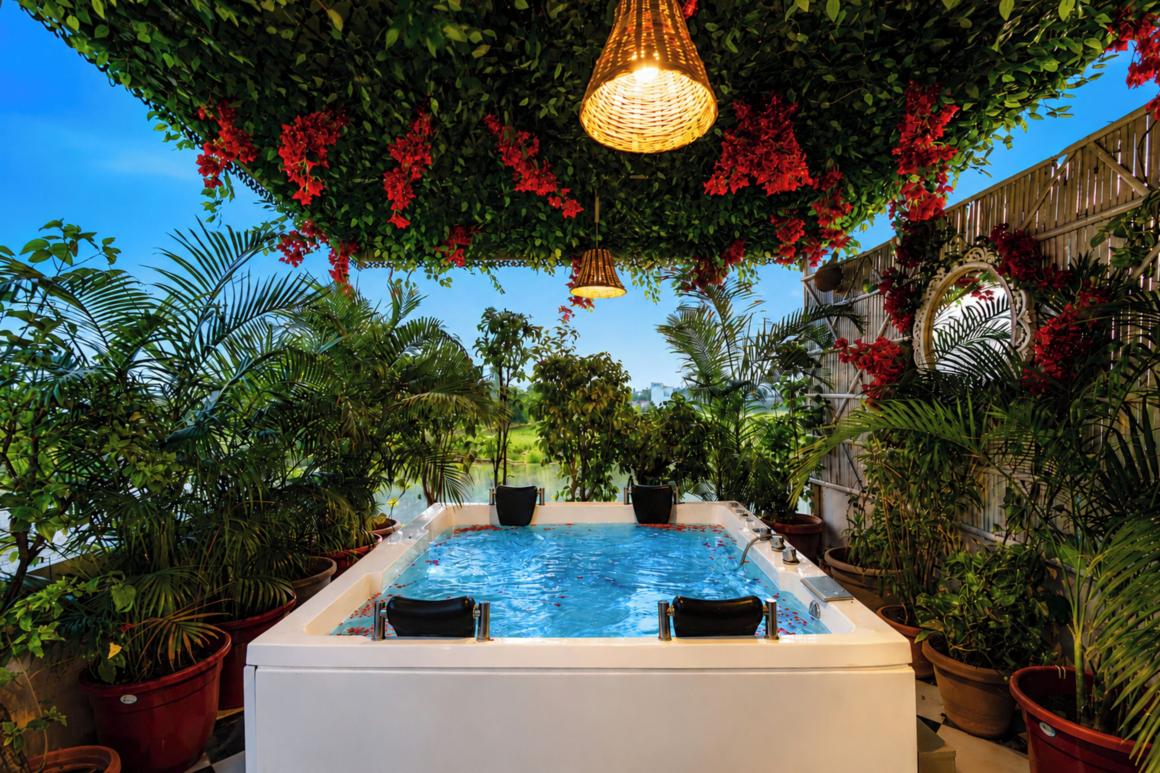 A hot tub surrounded by lush greenery and potted plants, with a clear blue sky in the background.