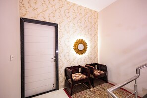 A hallway with a patterned wallpaper, a door, two wooden chairs with cushions, and a decorative mirror. - Alaya Stays Lamp house 3BHK Villa (Jaipur)