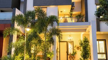 A modern two-story house with a balcony, potted plants, and a well-lit entrance.