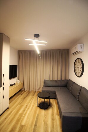 Ein modernes Wohnzimmer mit einem Ecksofa, einem runden Couchtisch, einem Flachbildfernseher und einer an der Wand befestigten Uhr.