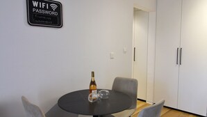 A modern dining area with a round table, two chairs, a bottle, and a sign indicating WIFI access. - STAY Aspri Petra Apartment (Paphos)