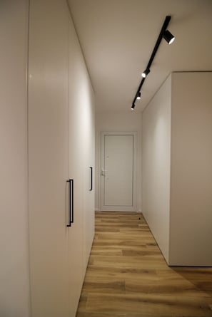 Un pasillo con piso de madera, paredes blancas y una puerta al final.