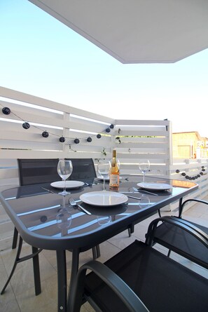 An outdoor dining area with a white pergola, black mesh chairs, and a glass table. - STAY Aspri Petra Apartment (Paphos)