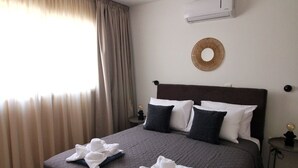 A hotel room with a large bed, a round mirror, an air conditioning unit, and a wooden floor. - STAY Aspri Petra Apartment (Paphos)