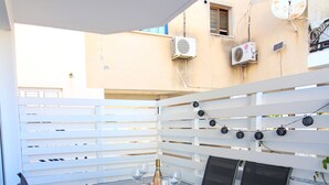 An outdoor patio with a table set for two, surrounded by chairs, and a white fence. - STAY Aspri Petra Apartment (Paphos)