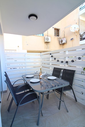 Un patio al aire libre con una mesa lista para dos personas, rodeado de sillas y una cerca blanca.