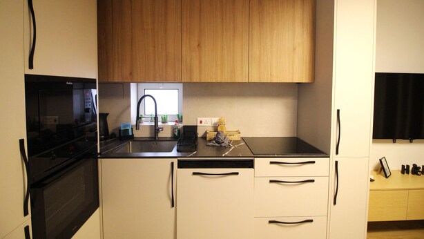 A compact kitchen with a black countertop, wooden cabinets, a built-in oven, and a window above the sink. - STAY Aspri Petra Apartment (Paphos)