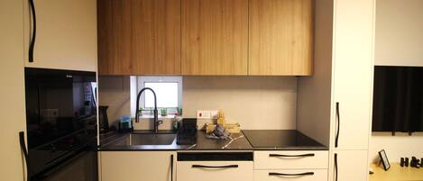 A compact kitchen with a black countertop, wooden cabinets, a built-in oven, and a window above the sink.