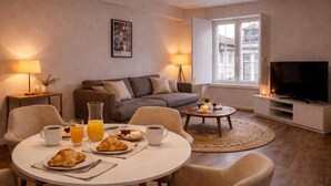 A modern living room with a round dining table, sofas, a TV, and a window with a view of buildings. - Praça do Comércio Romantic Apartment (Lisboa)