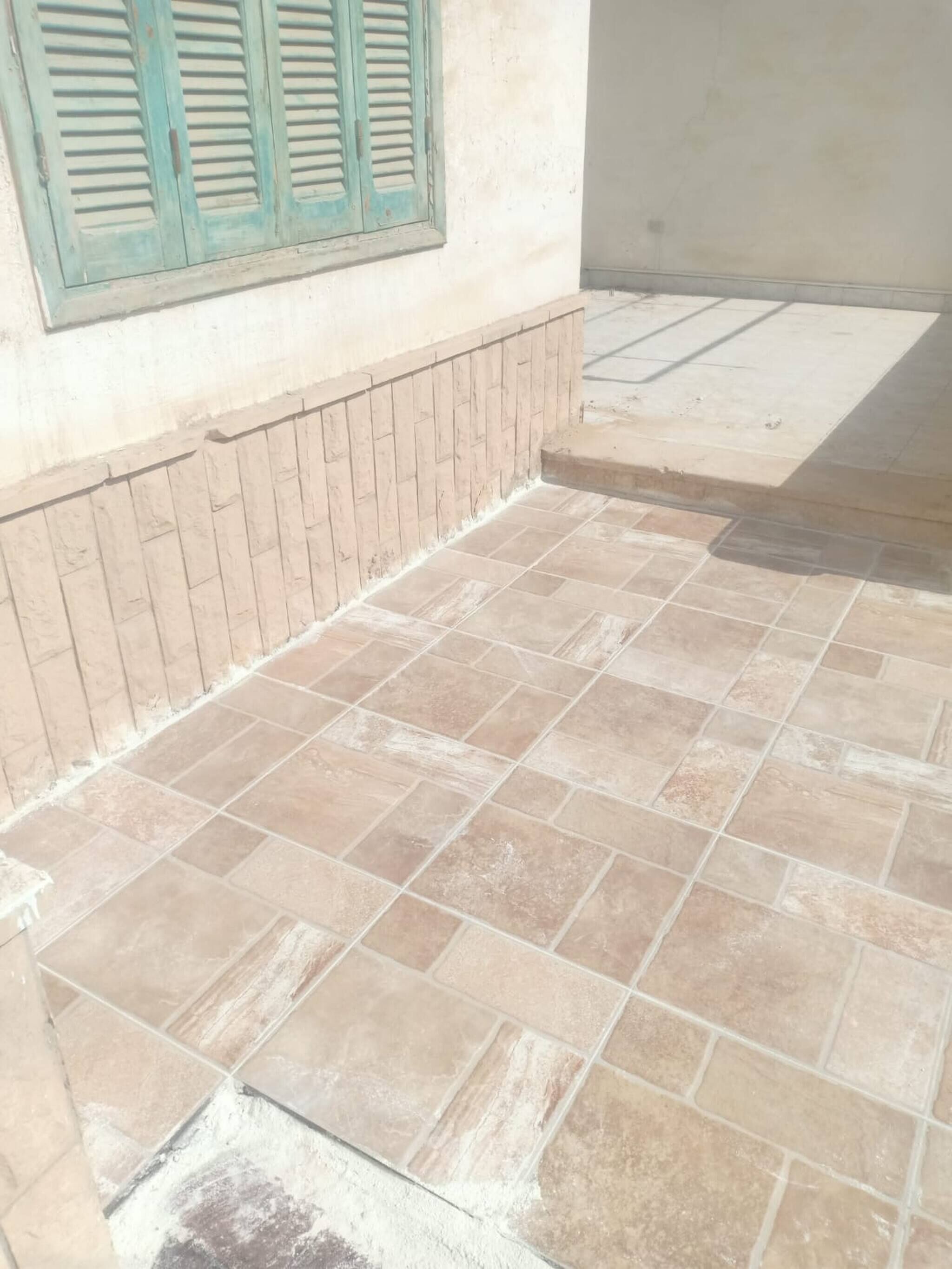 Una zona con pavimento piastrellato, un muro in mattoni e una finestra con persiane.