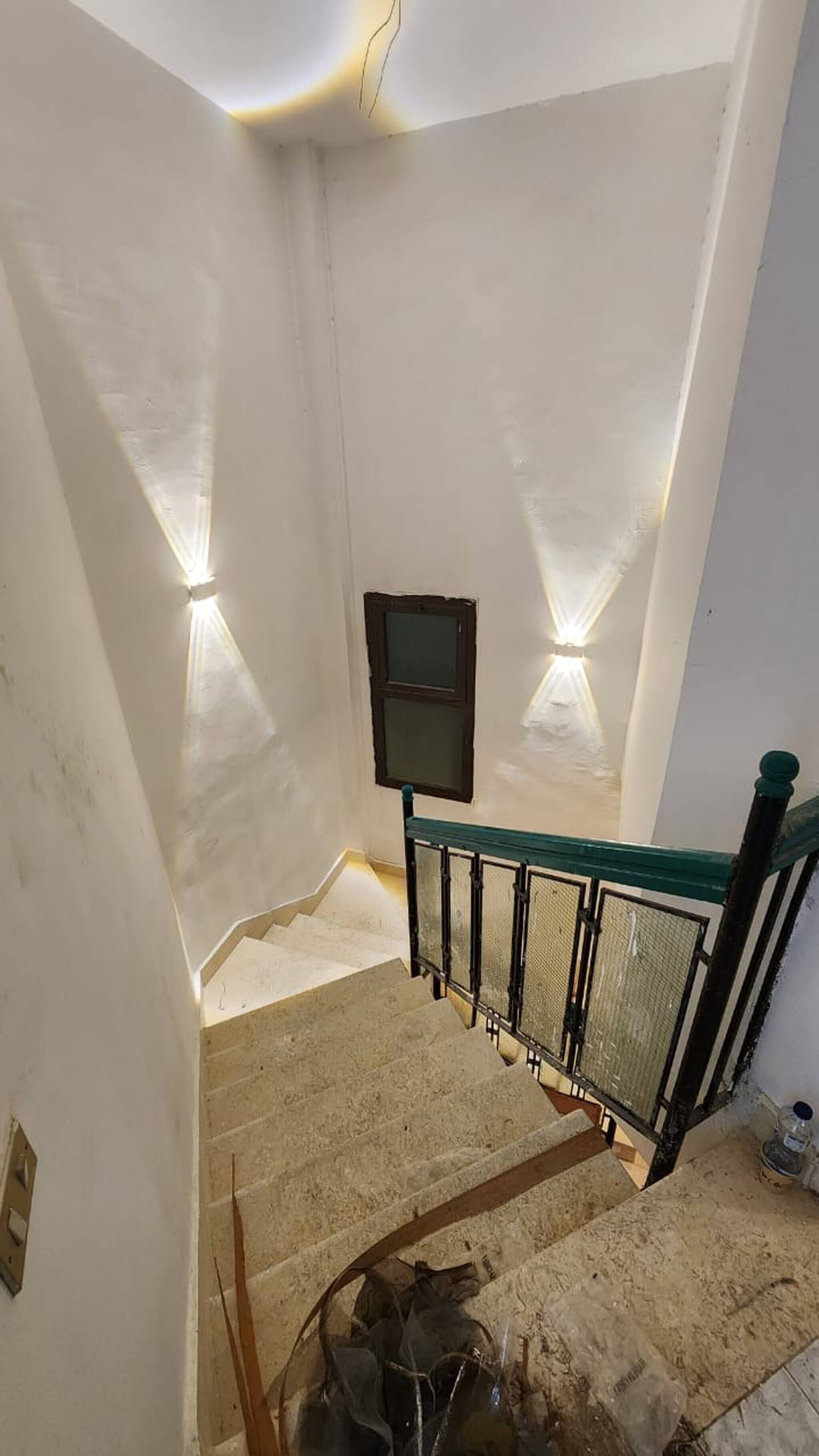 A staircase with a handrail, a wall-mounted light fixture, and a window with a dark frame.
