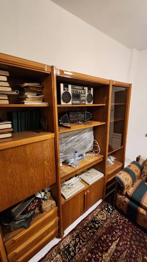 Una estantería de madera con libros, un radio y dispositivos electrónicos.