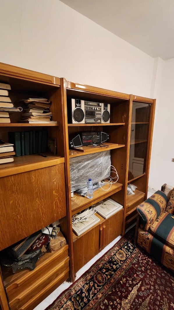 A wooden bookshelf with books, a radio, and electronic devices.