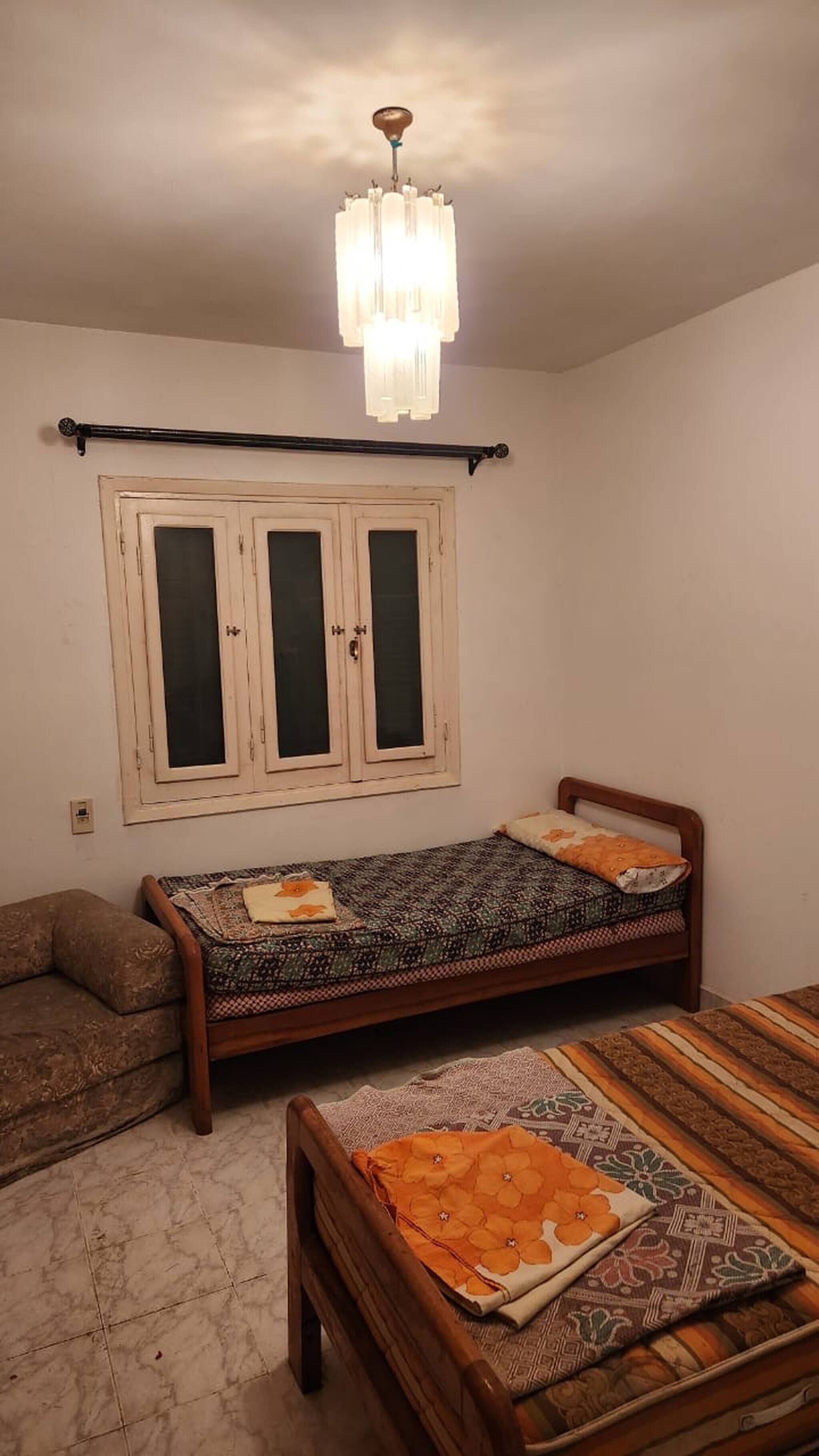 Une pièce comprenant un lit, un canapé, une fenêtre avec des rideaux et un lustre.