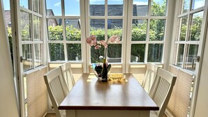 Een eethoek met een tafel en stoelen, grote ramen en uitzicht op groen.