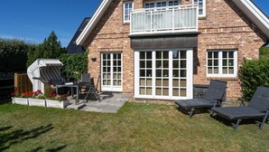 Een bakstenen huis met een balkon, een terras met een tafel en stoelen, en een tuin.