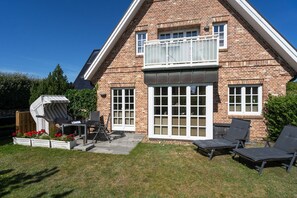 Ein Backsteinhaus mit Balkon, einer Terrasse mit Tisch und Stühlen und einem Garten.