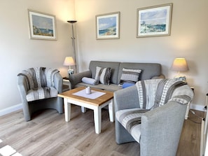 A living room with a grey sofa, two armchairs, a coffee table, and three framed artworks on the wall. - Eidumweg Apartment 3 - Bright and modern ground-floor apartment for 2 people with (Sylt)