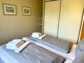 A hotel room with two beds, each with striped bedding and folded towels. There are two framed pictures on the wall. - Eidumweg Apartment 3 - Bright and modern ground-floor apartment for 2 people with (Sylt)