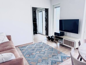 Ein modernes Wohnzimmer mit Flachbildfernseher, Couchtisch, Sofa und einem gemusterten Teppich.