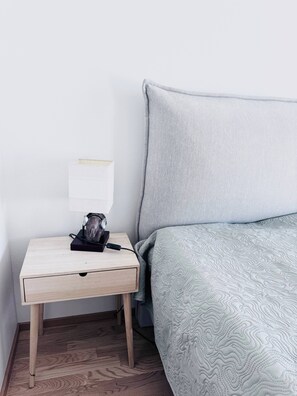 A neatly made bed with a patterned blanket, a bedside table with a lamp, and a power adapter. - Nordic Home Bliss with Sports (Helsinki)
