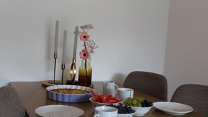 Ein Esstisch mit Obstschale, Kuchen und Blumen in einer Vase.