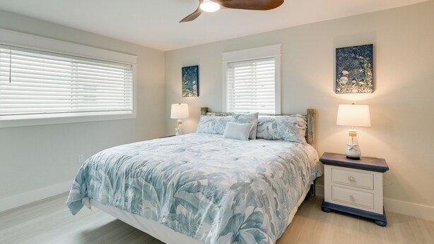 A bedroom with a bed, two bedside tables, a ceiling fan, and artwork on the walls. - Walk to Englewood Beach! Resort-Style Villa (Englewood)