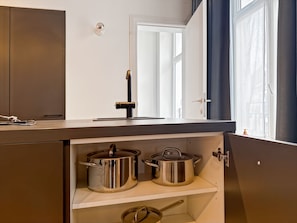 A kitchen with a built-in stove, two stainless steel pots, and a window with curtains. - self check in 2 bedroom in Brussels (Ixelles)