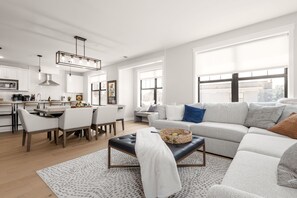 Ein modernes Wohnzimmer mit einem grauen Sofa, einem Essbereich mit weißen Stühlen und einer Küche mit weißen Schränken.