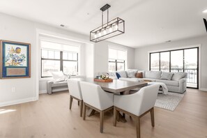 Un salon spacieux avec une grande fenêtre, un coin repas avec une table et des chaises en bois, et un lustre moderne.