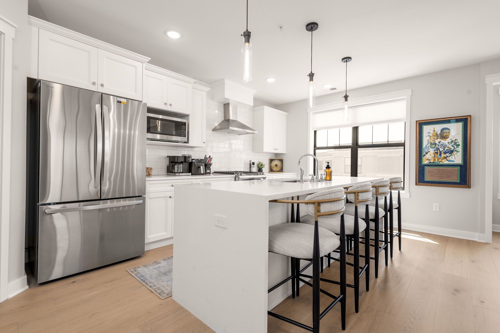 A modern kitchen with stainless steel appliances, a central island with bar stools, and pendant lighting.