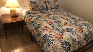 Una cama individual con colcha estampada, una lámpara de noche y una mesita de madera.