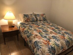 Ein Einzelbett mit floralem Überwurf, eine Nachttischlampe und ein Nachttisch aus Holz.
