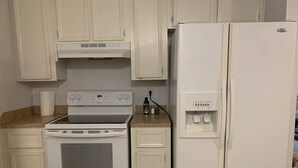 Una cocina con armarios blancos, una estufa blanca y un refrigerador blanco.
